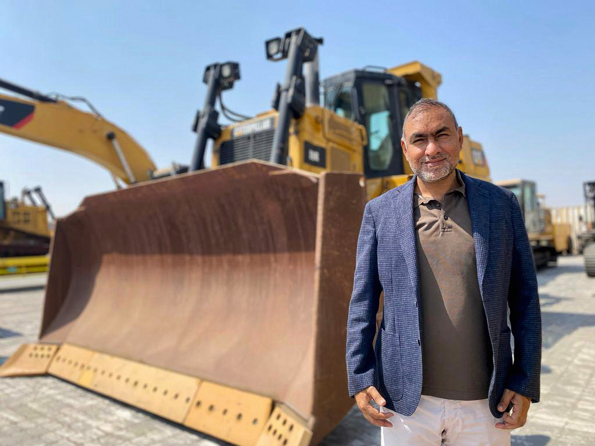 Mr. Hussein is standing in front of the heavy equipment