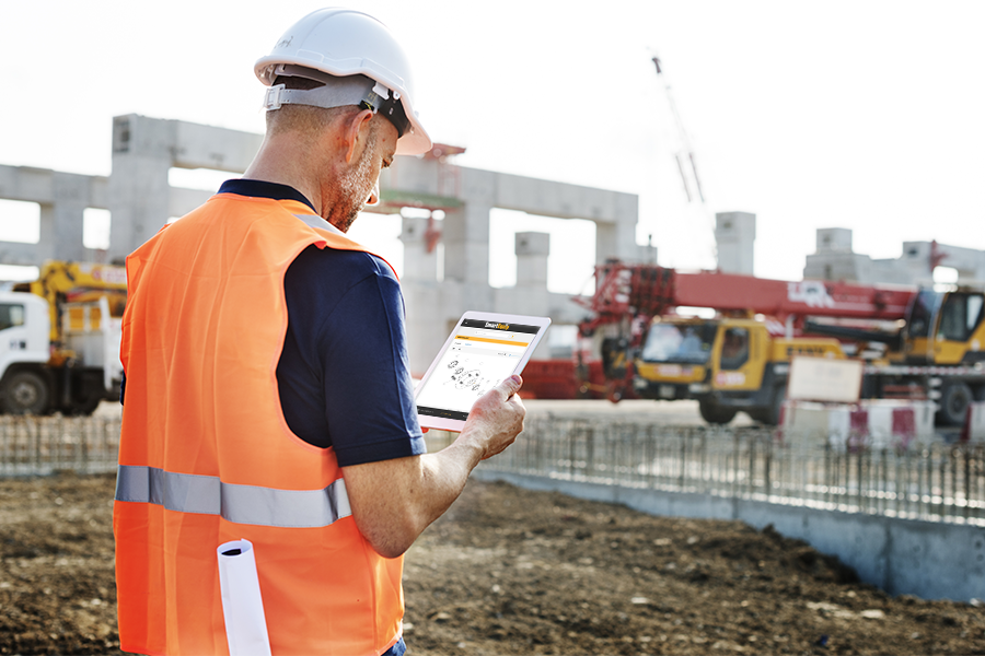 A man with a hard hat, and high-visibility jacket looking at his tablet in the construction site.