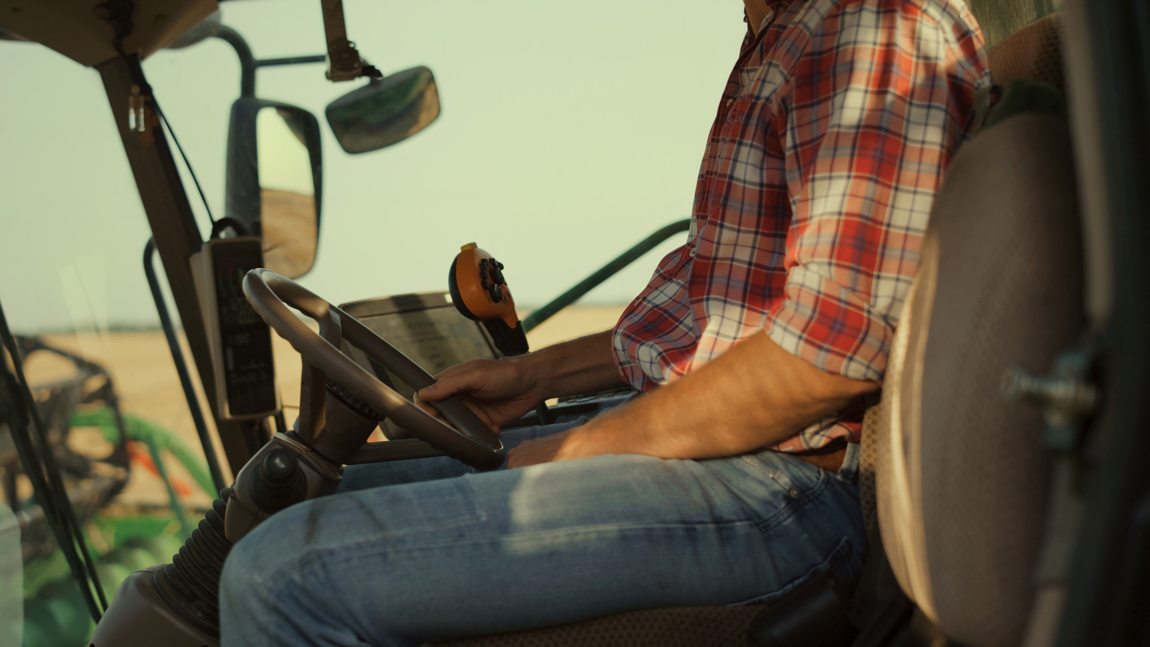 A man wearing pants and red checkered sleeves drives a machine equipment.