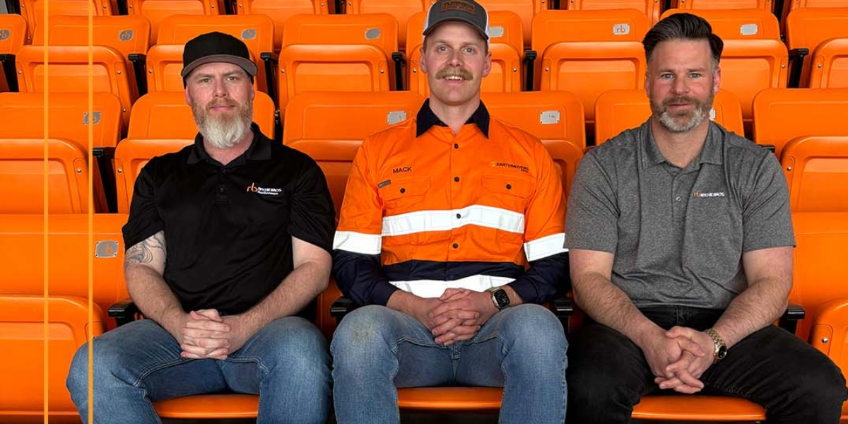 Mack Plovie, sitting in a row of orange stadium seats with two gentlemen from Ritchie Bros.