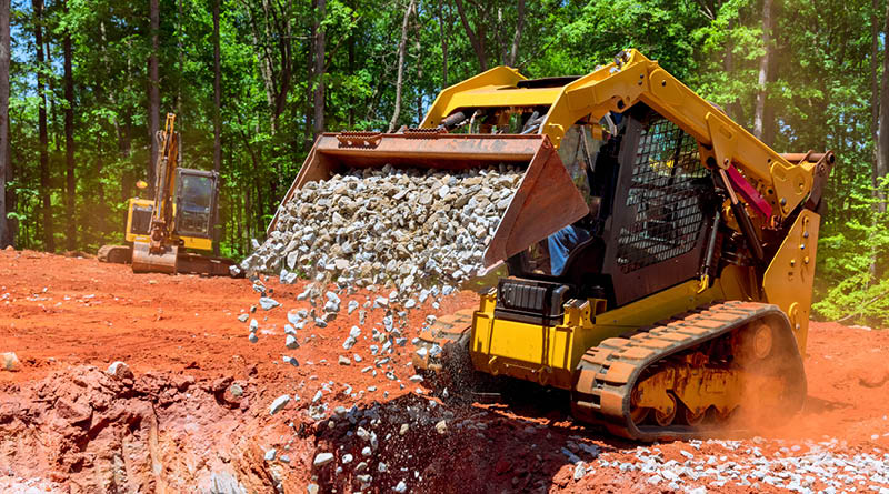 A compact track loader moving crushed stone.