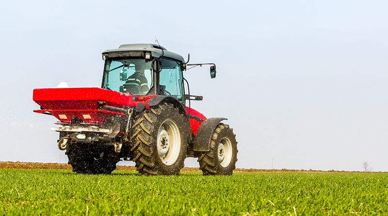 An agricultural tractor with a fertilizer spreader is parked in the field.