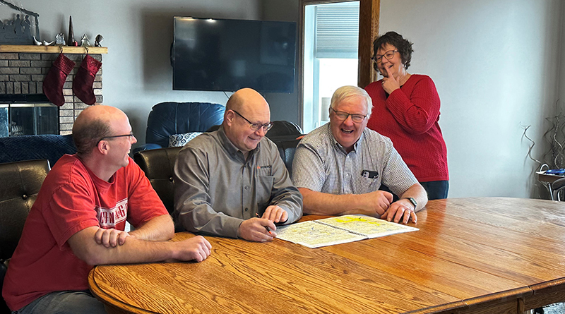 Three gentlemen and a woman are smiling in the boardroom.